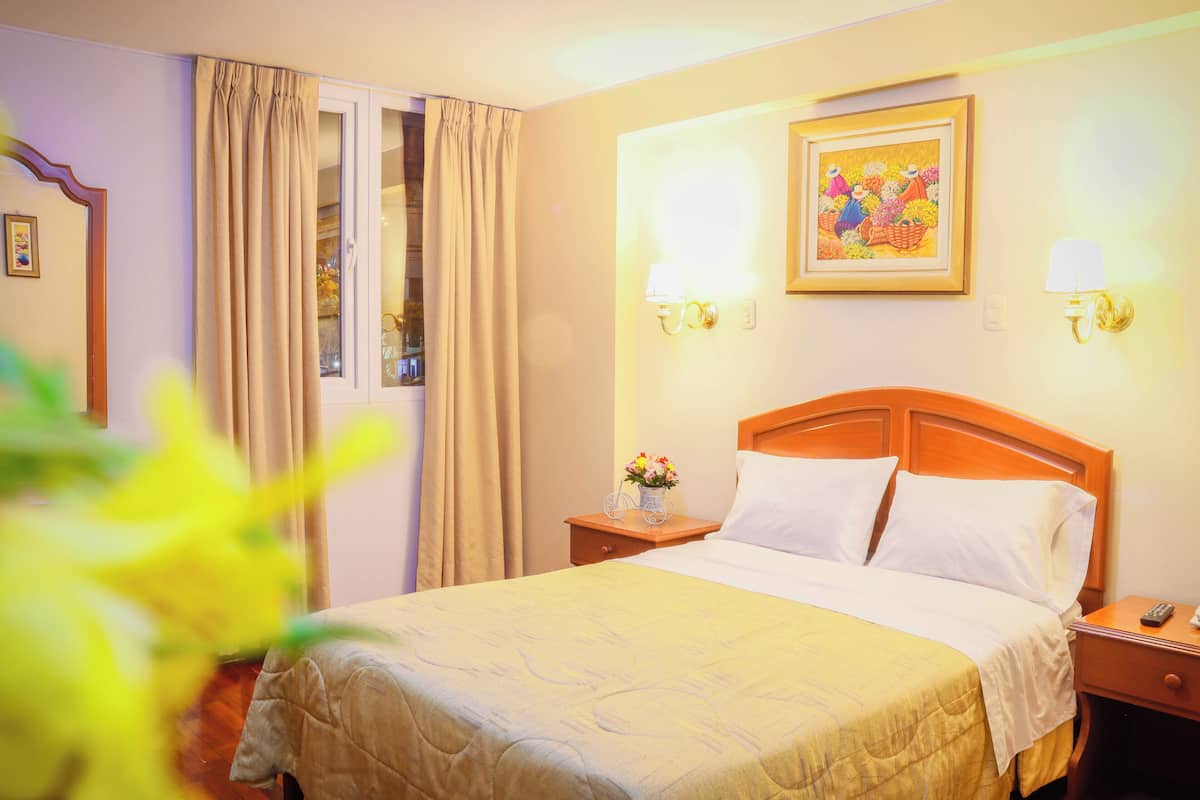 Une chambre d’hôtel comprenant un lit, des tables de chevet, une fenêtre avec des rideaux et des lampes fixées au mur.