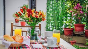 Uma mesa de café da manhã com pão, um vaso de flores e um copo de suco de laranja.