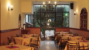 Uma área de refeições com mesas e cadeiras, um candelabro e uma janela grande com vista para o verde.