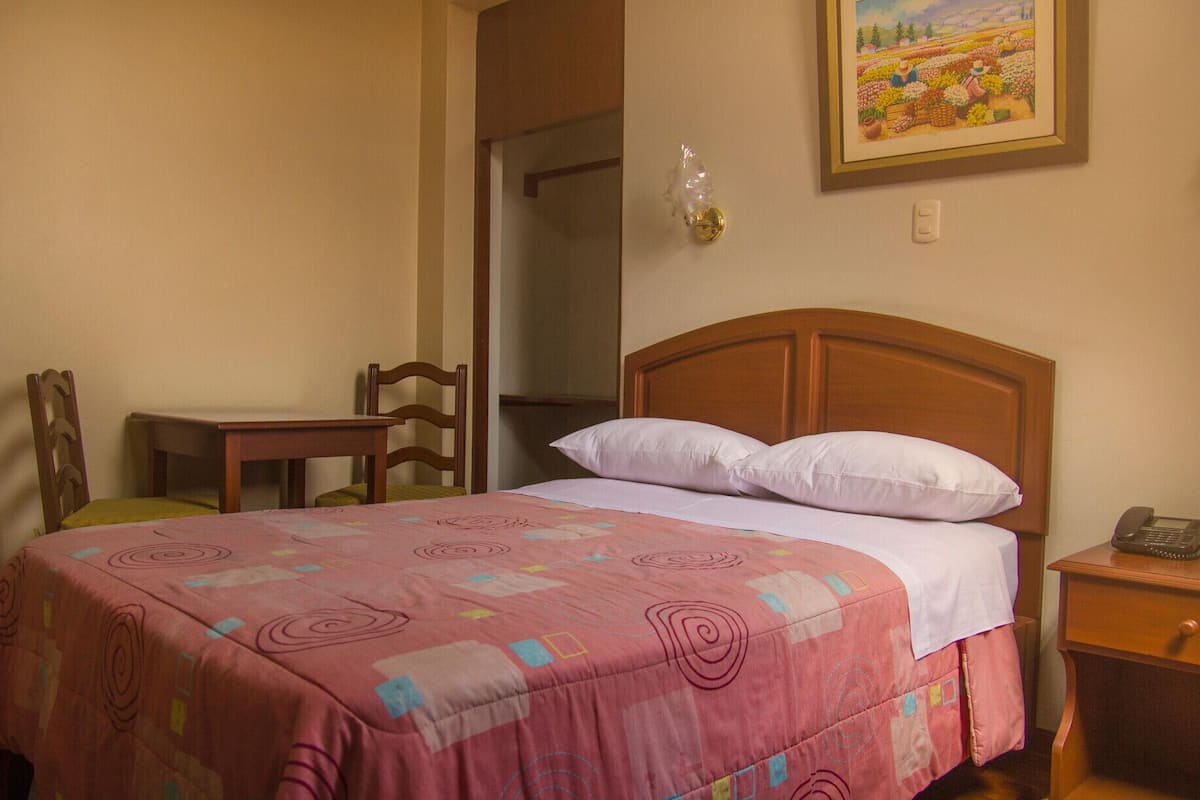 Une chambre à coucher comprenant un lit, une chaise, une table de chevet et un luminaire fixé au mur.