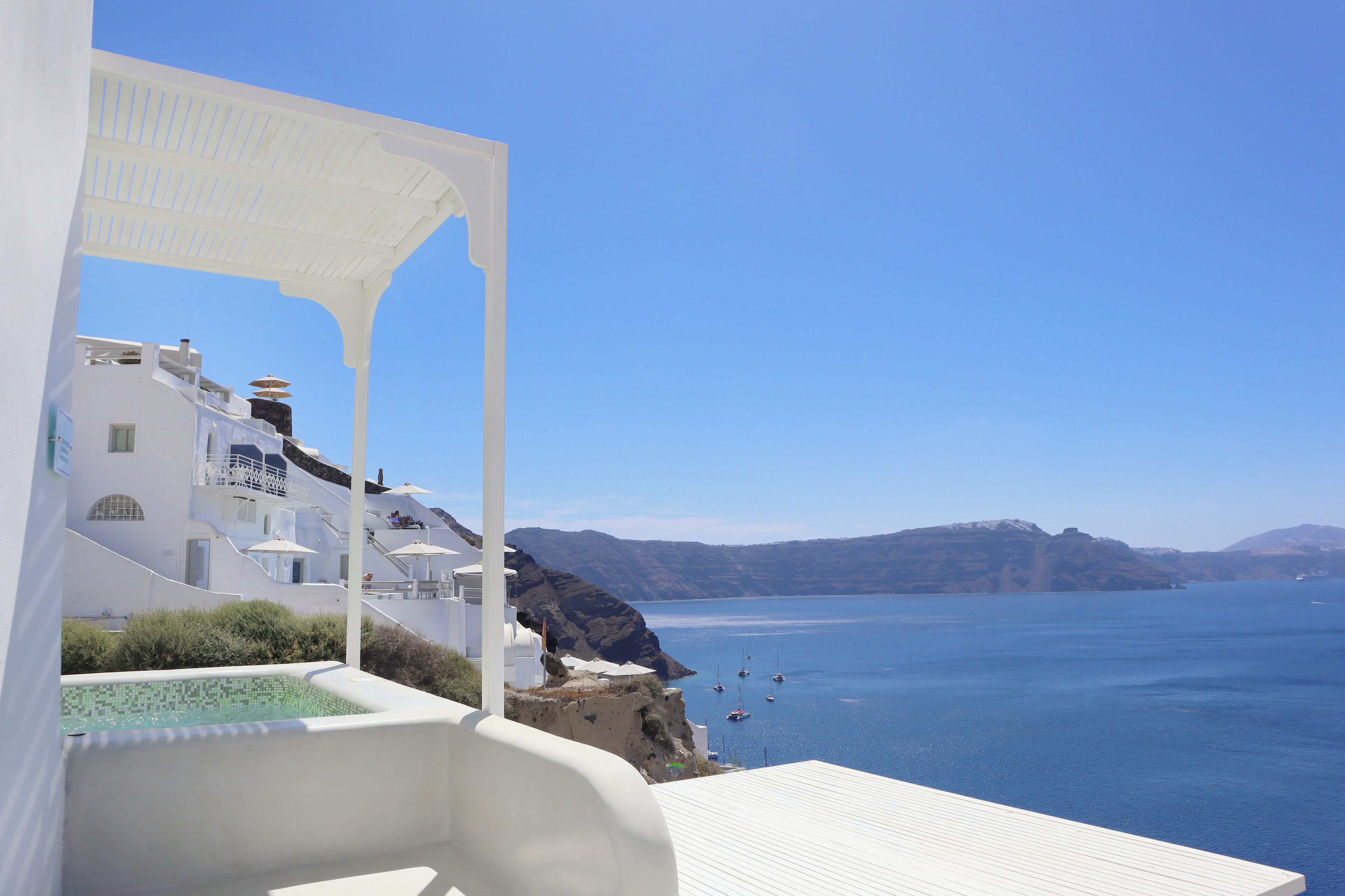 A white building with a pool, a white pergola, and a view of the sea.