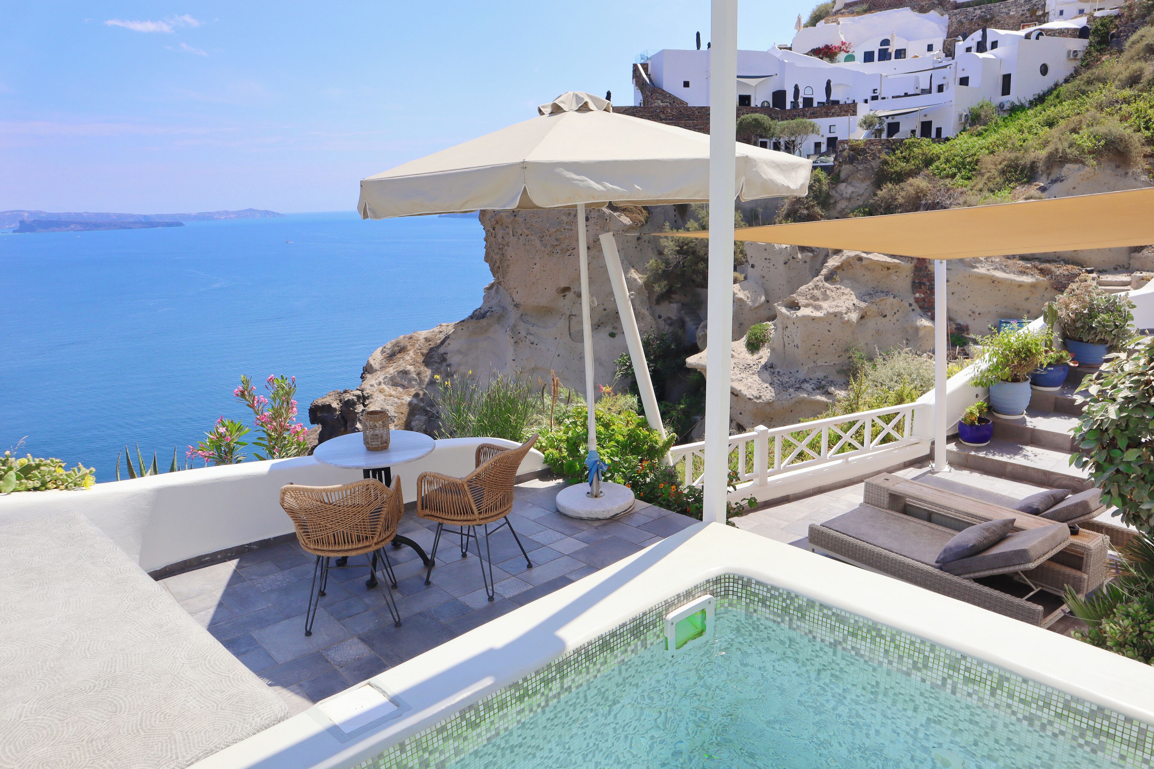 Zona de piscina con sillas de descanso y una mesa, con vista a un acantilado y al mar.