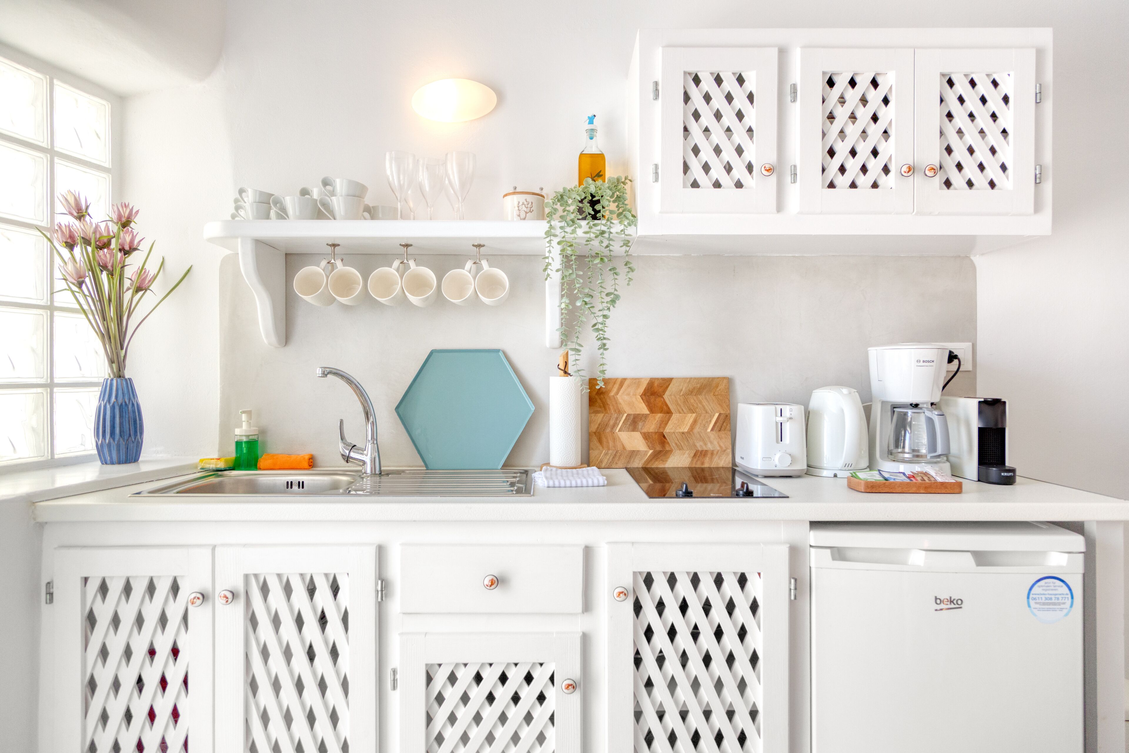 Una cocina moderna con armarios blancos, lavavajillas integrado y cafetera.