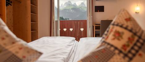 Un dormitorio con dos camas, un televisor montado en la pared y una ventana con vistas a las montañas.