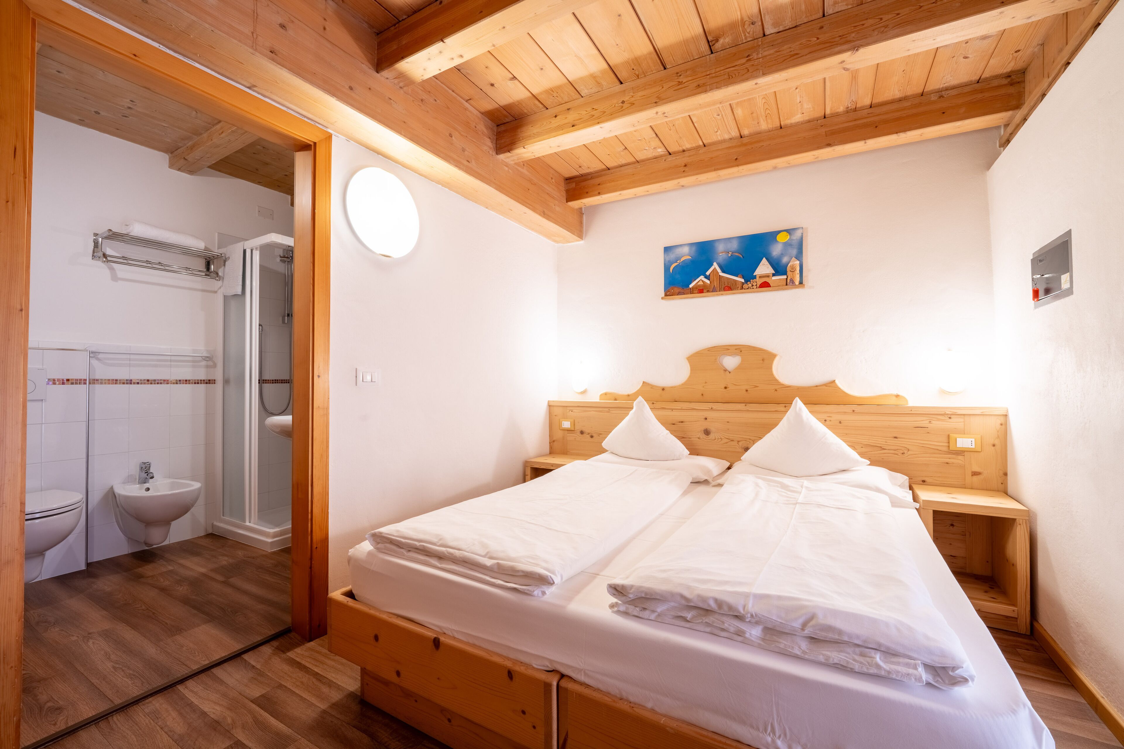 A bedroom with a wooden headboard, a double bed, a nightstand, and a painting on the wall.
