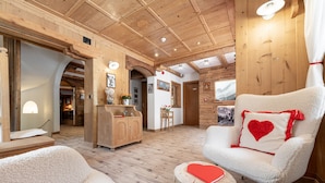 Una habitación acogedora con vigas de madera, un sillón mullido con un cojín con forma de corazón, un armario de madera y una mesita con un corazón rojo.