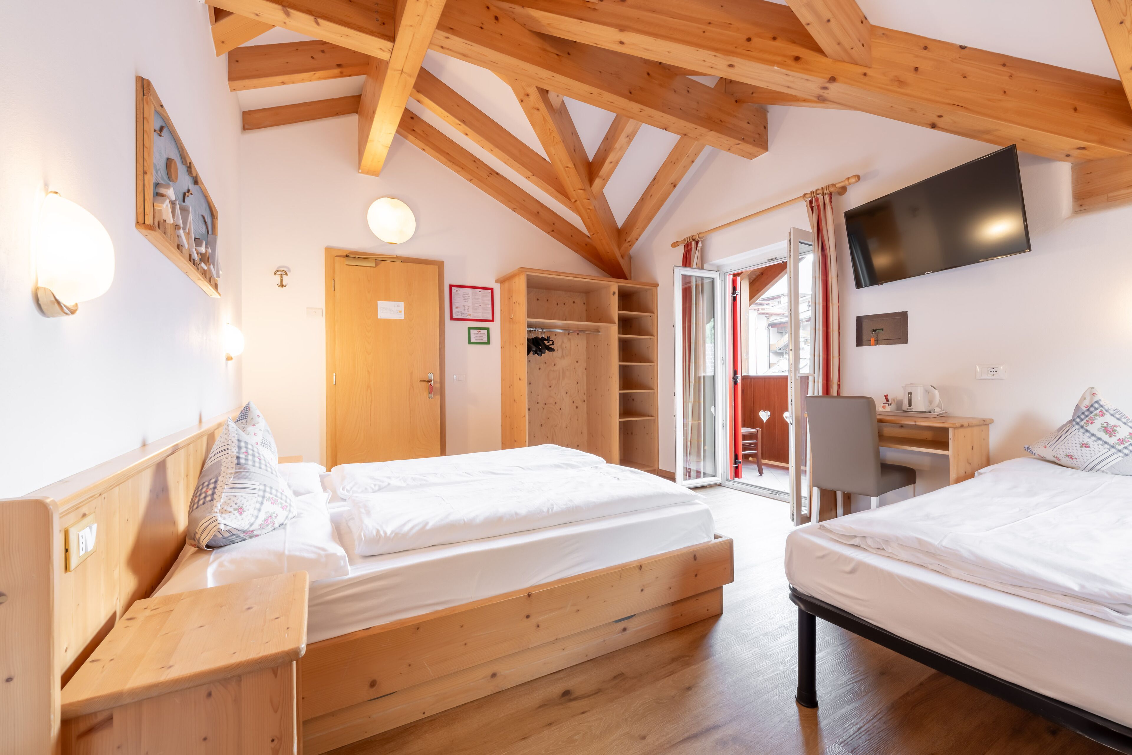A room with two wooden beds, a desk, a chair, a TV, and a wardrobe.