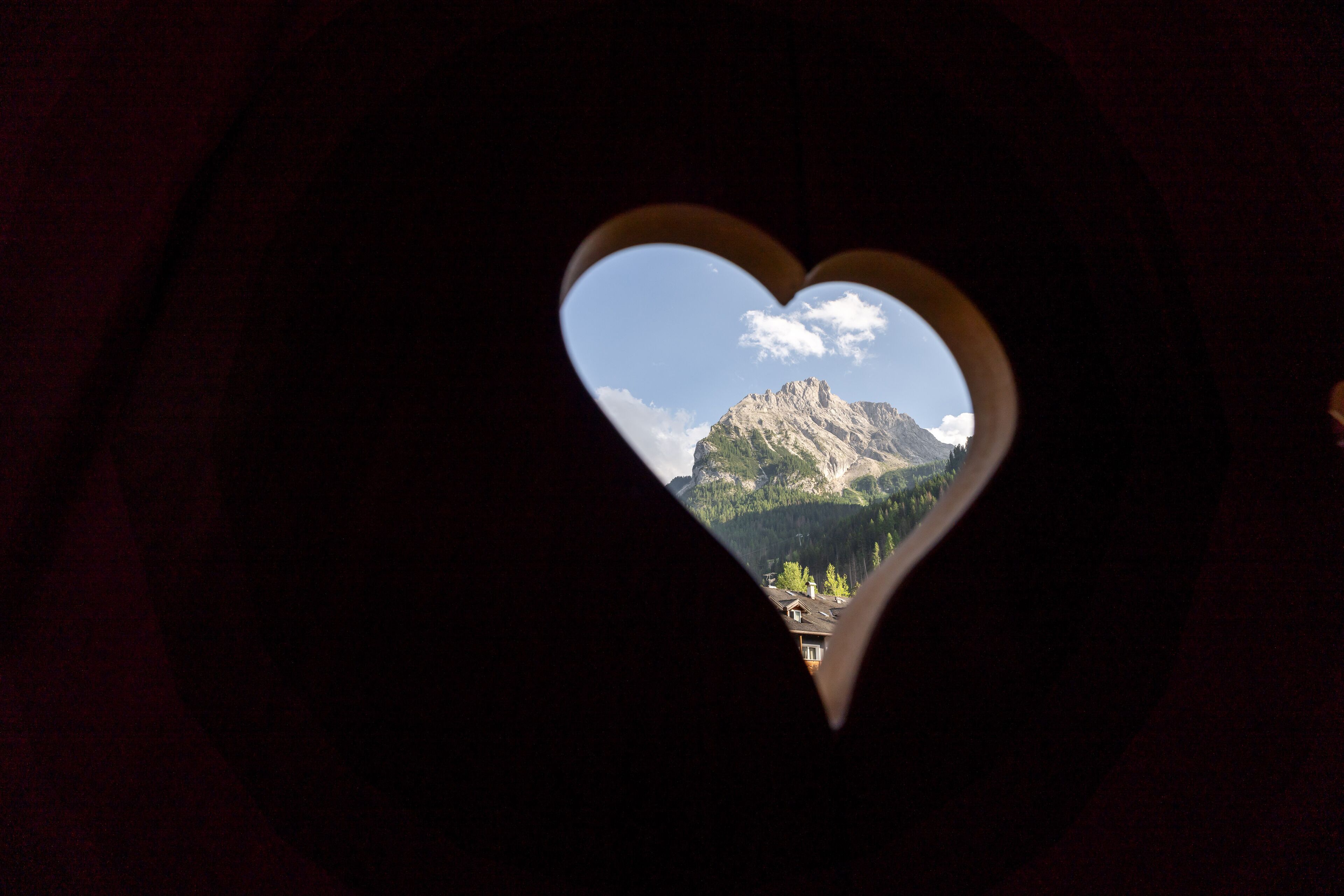 A heart-shaped window with a view of a mountain and a small village.
