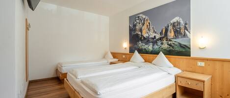 Un dormitorio con dos camas de madera, una mesita de noche, un televisor montado y un cuadro de un paisaje montañoso.