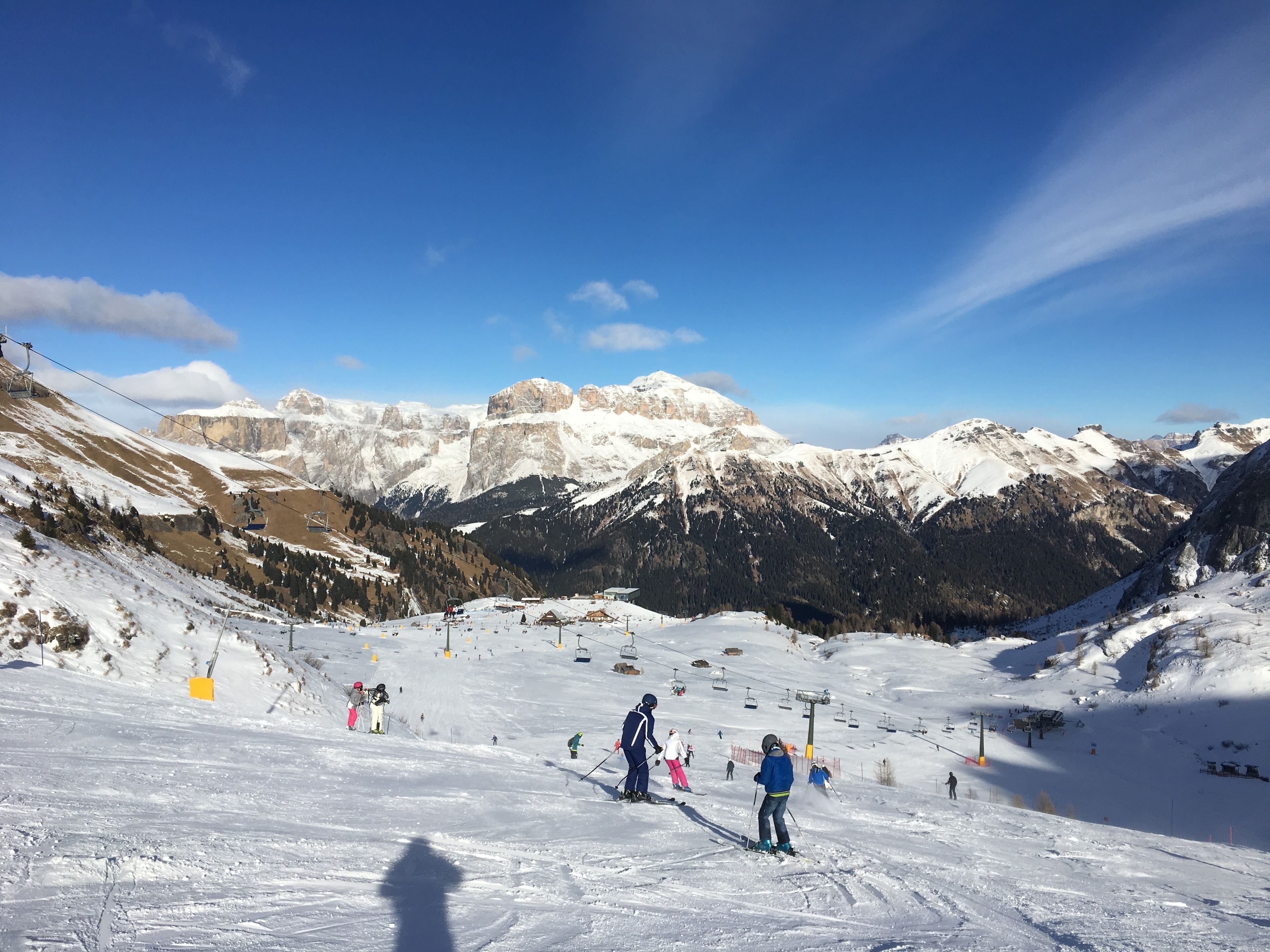 Une piste de ski avec des skieurs, un télésiège et des montagnes enneigées en arrière-plan.