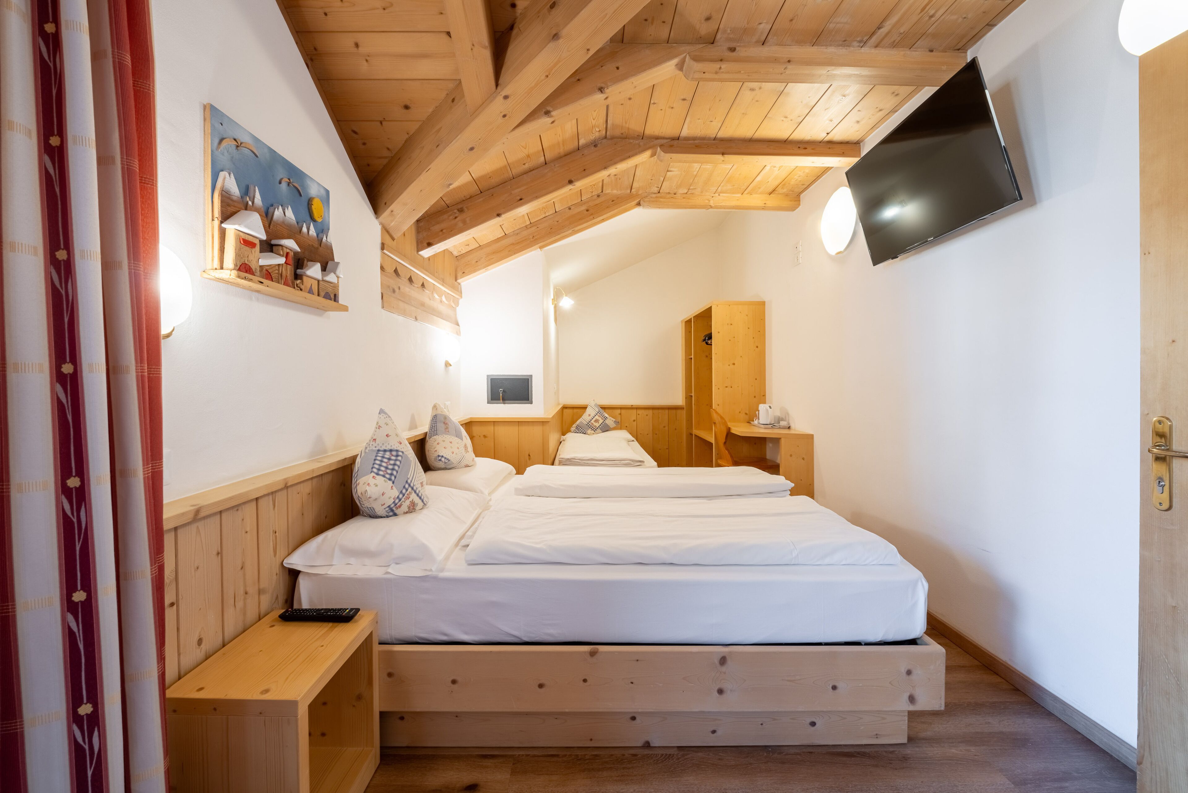 A bedroom with a wooden ceiling, a bed with white bedding, a mounted TV, and a painting on the wall.