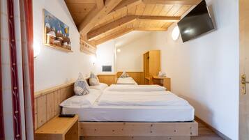 A bedroom with a wooden ceiling, a bed with white bedding, a mounted TV, and a painting on the wall.