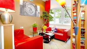 A red and beige room with a sofa, a lamp, a bookshelf, and a window. - Hotel Charles Central - Czech Leading Hotels (Prague)