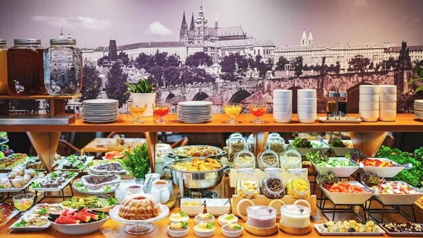 A buffet with various food items and beverages, with a cityscape backdrop. - Hotel Charles Central - Czech Leading Hotels (Prague)