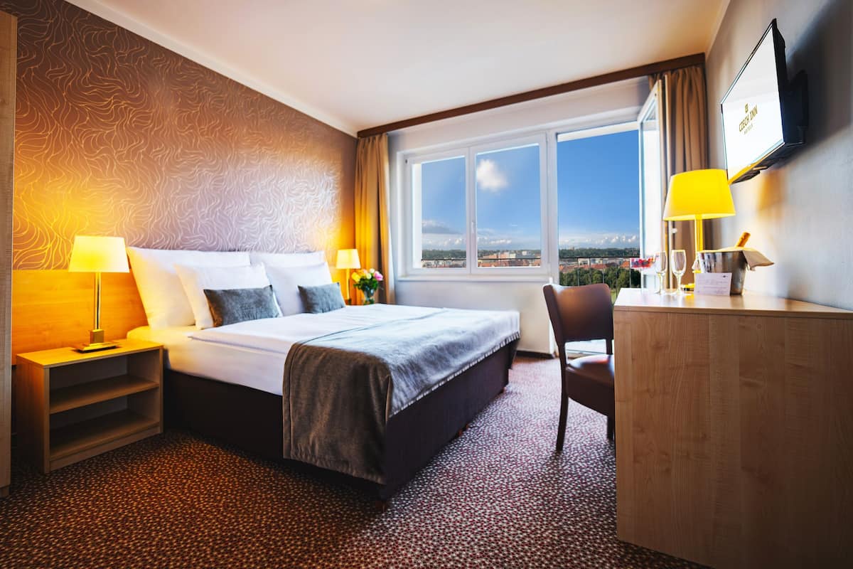 A hotel room with a bed, a desk, a chair, a TV, and a window with a city view.