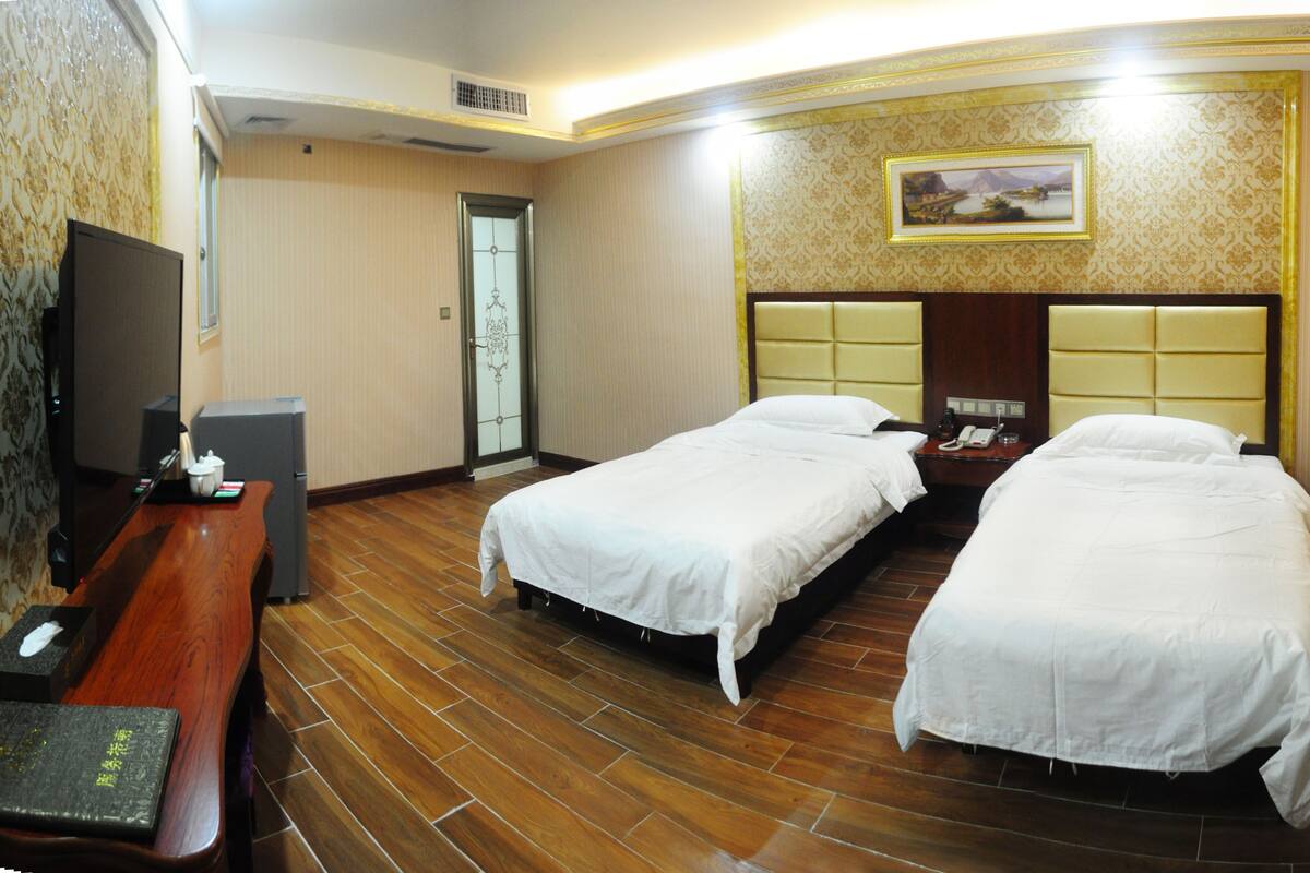 A hotel room with two beds, a wooden floor, a TV, and a painting on the wall.