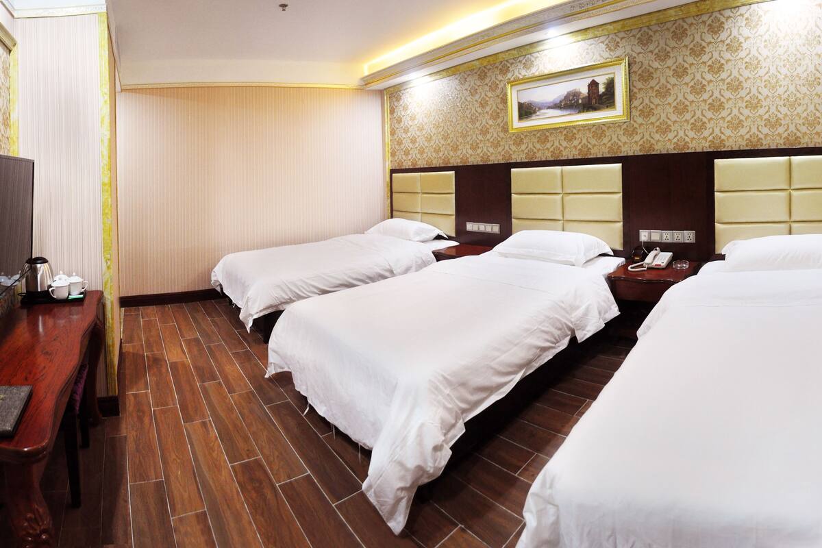 A hotel room with three single beds, a wooden desk with a telephone, and a television.