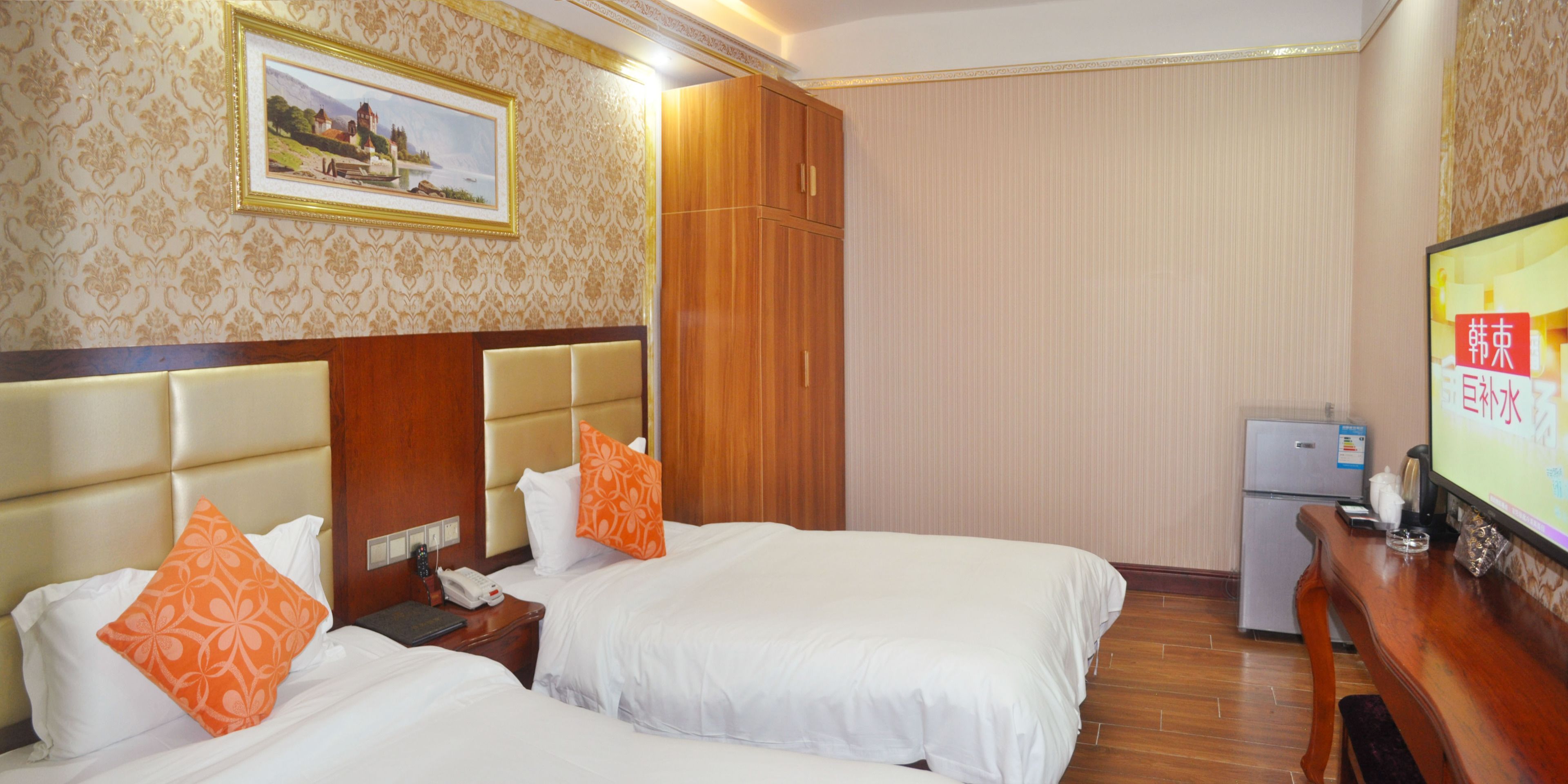 A hotel room with two beds, a wooden wardrobe, a television, and a small refrigerator.