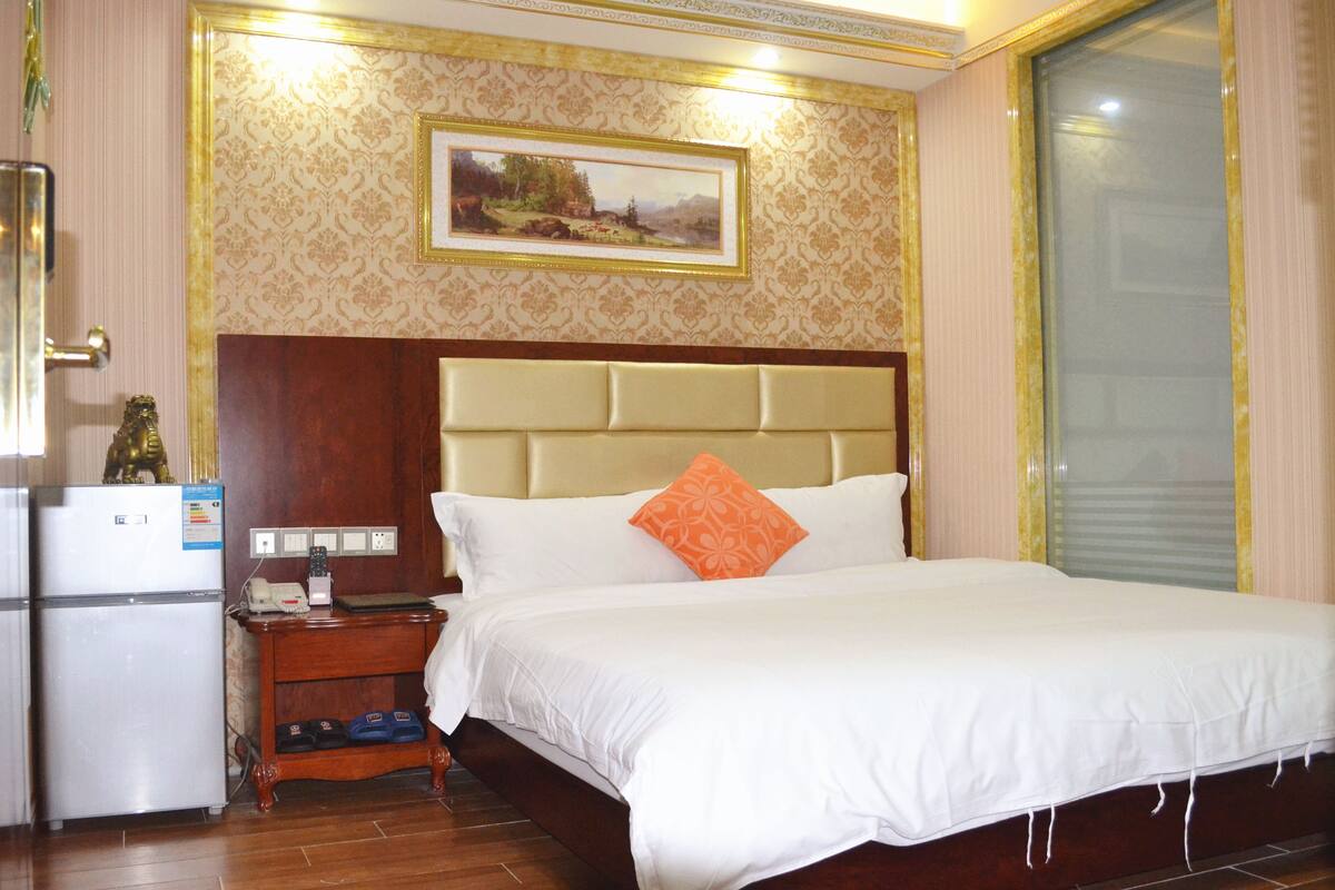 A hotel room with a bed, nightstand, and a refrigerator.