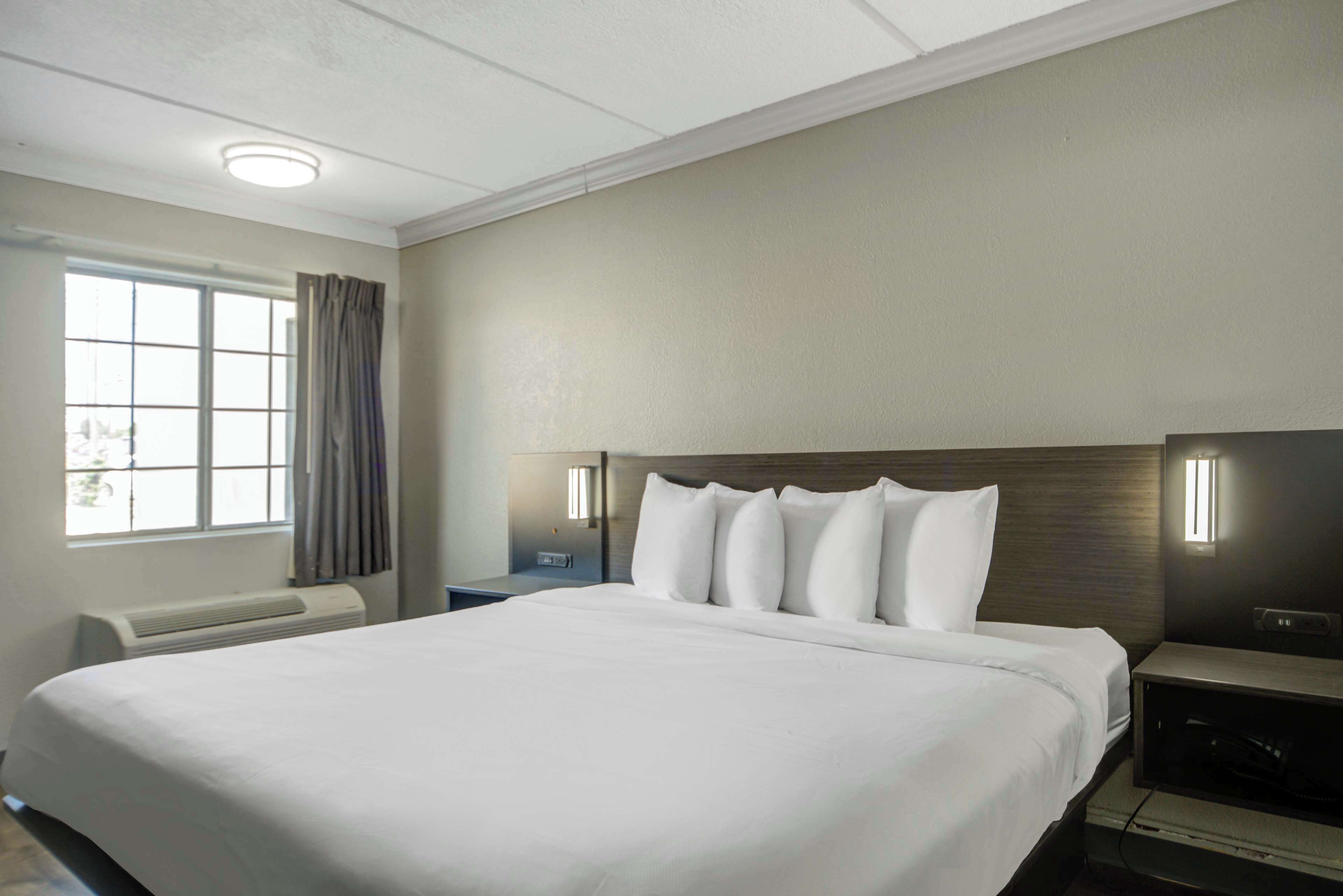 A hotel room with a large bed, a nightstand, a lamp, and a window with curtains.