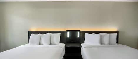 A hotel room with two single beds, a dark wood floor, and a light-colored wall.