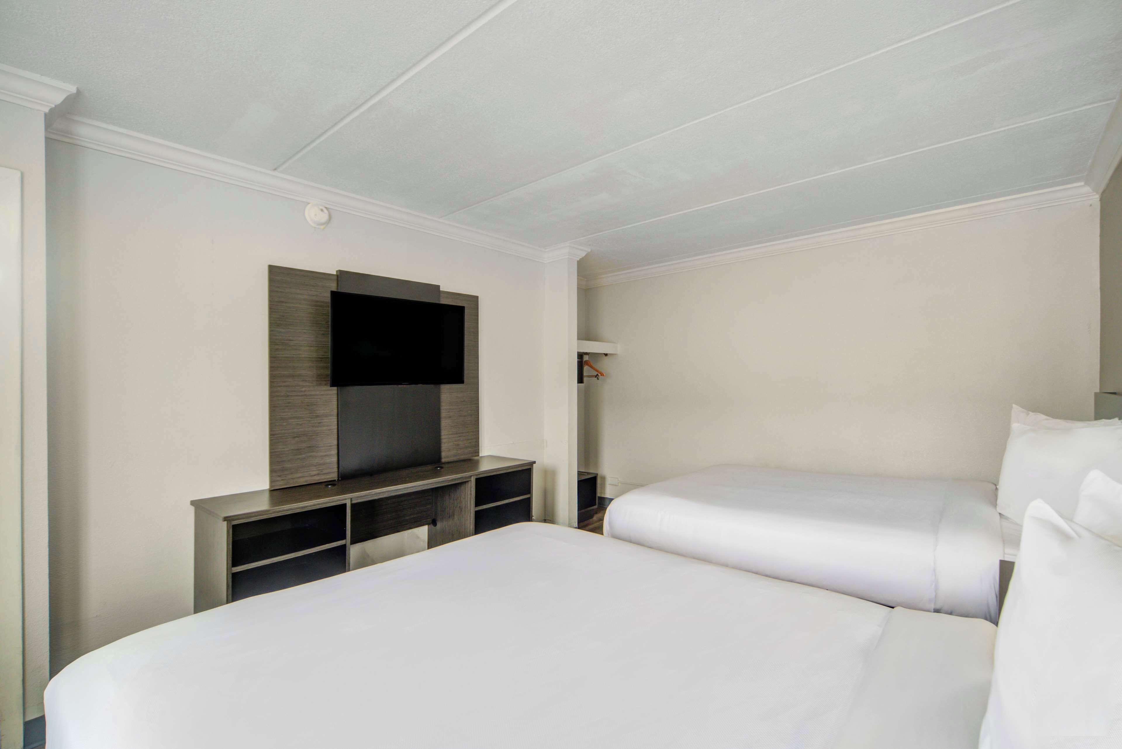Habitación de hotel con dos camas, un televisor de pantalla plana montado en un panel de madera y un estante pequeño con un espejo.