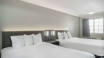 Habitación de hotel con dos camas, una mesita de noche, una lámpara de pared y una ventana con cortinas.