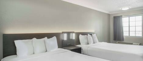 A hotel room with two beds, a nightstand, a wall-mounted lamp, and a window with curtains.