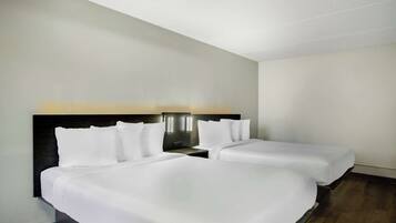 Habitación de hotel con dos camas individuales, cabecera oscura y mesita de noche con lámpara.