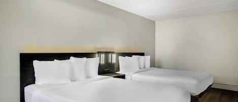 A hotel room with two single beds, a dark headboard, and a nightstand with a lamp.