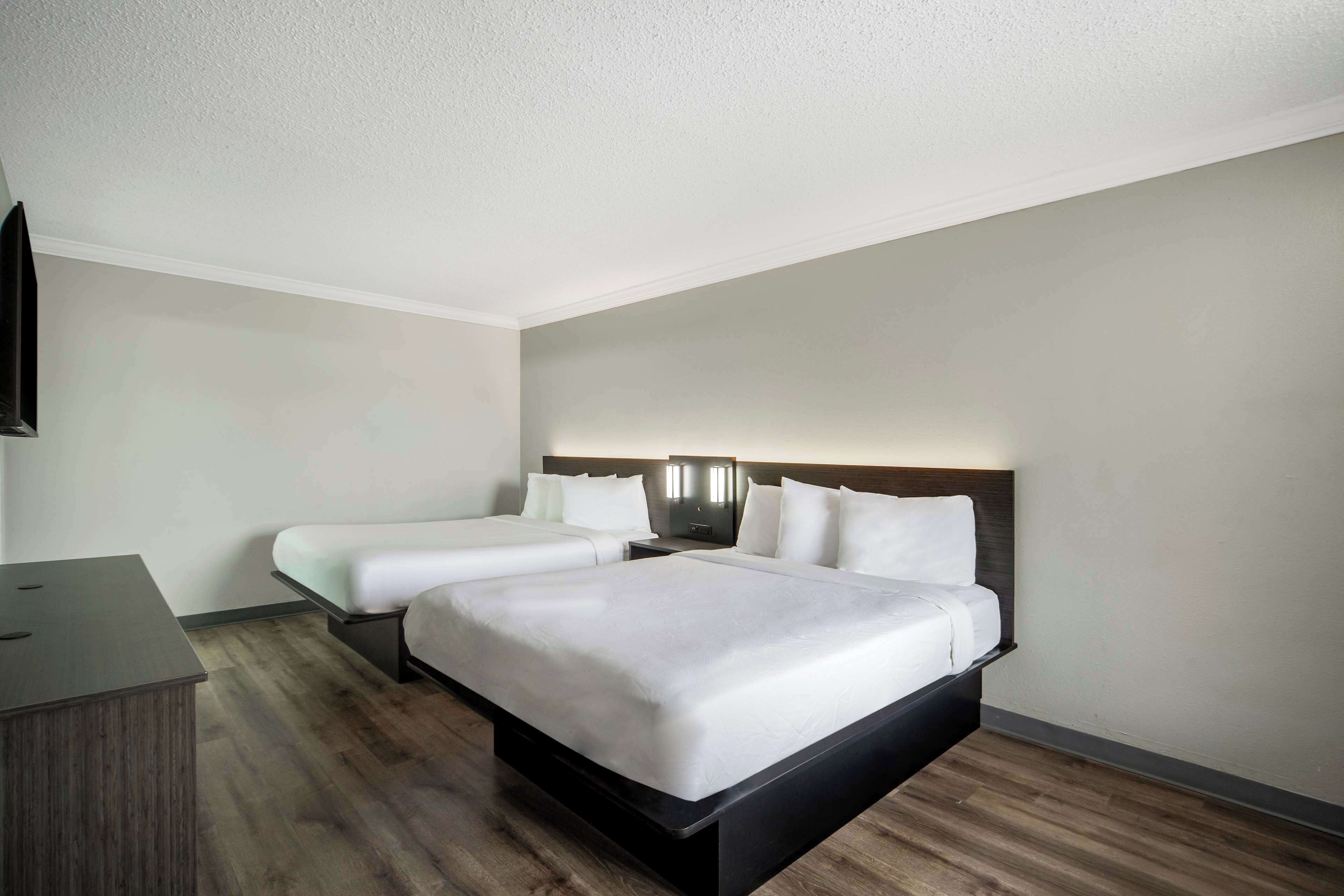 A hotel room with two single beds, a desk, and a flat-screen TV.