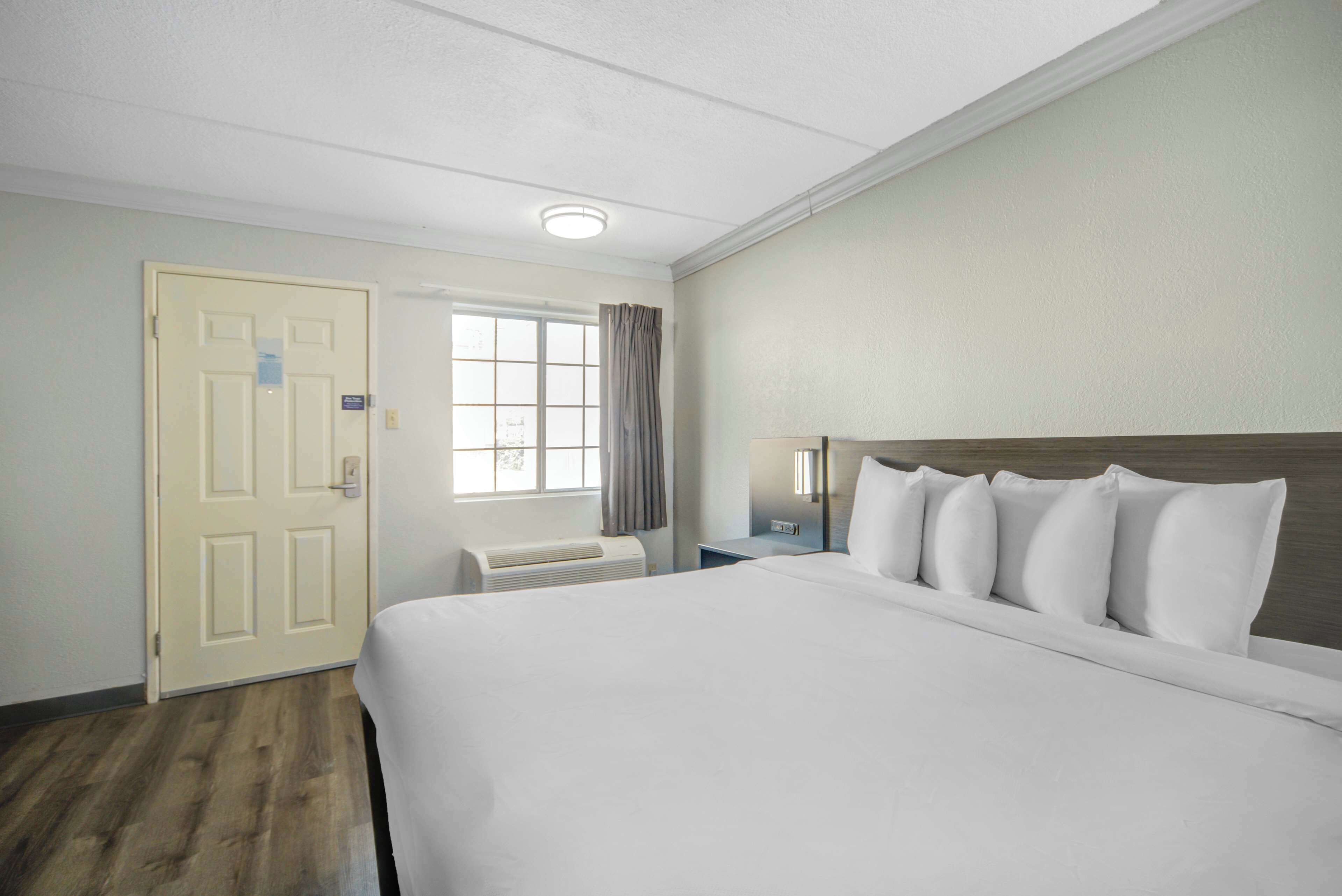 A hotel room with a large bed, a window with curtains, a nightstand, and a wall-mounted lamp.