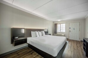 A hotel room with a large bed, a bedside table with a radio, a nightstand, a window with curtains, and a door. - Motel 6 San Antonio, TX – I-35 North Corridor (San Antonio)