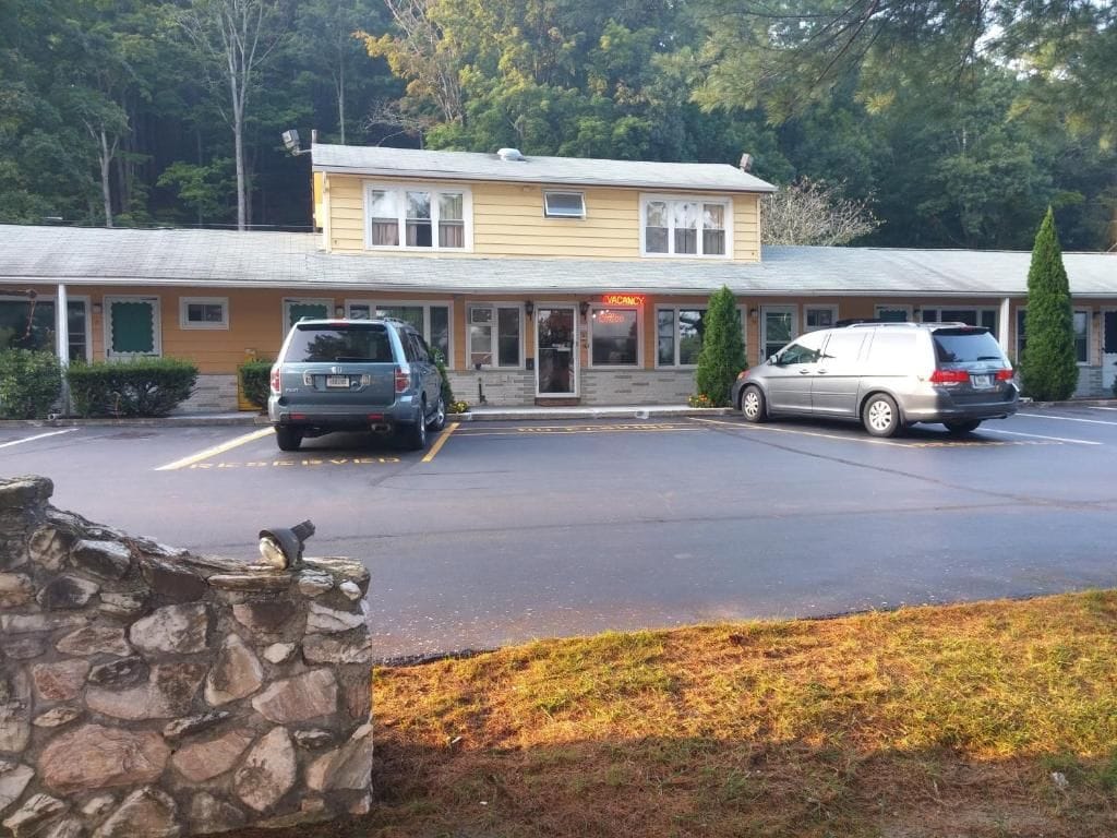 A motel with a two-story structure, a parking lot, and a stone wall in the foreground.