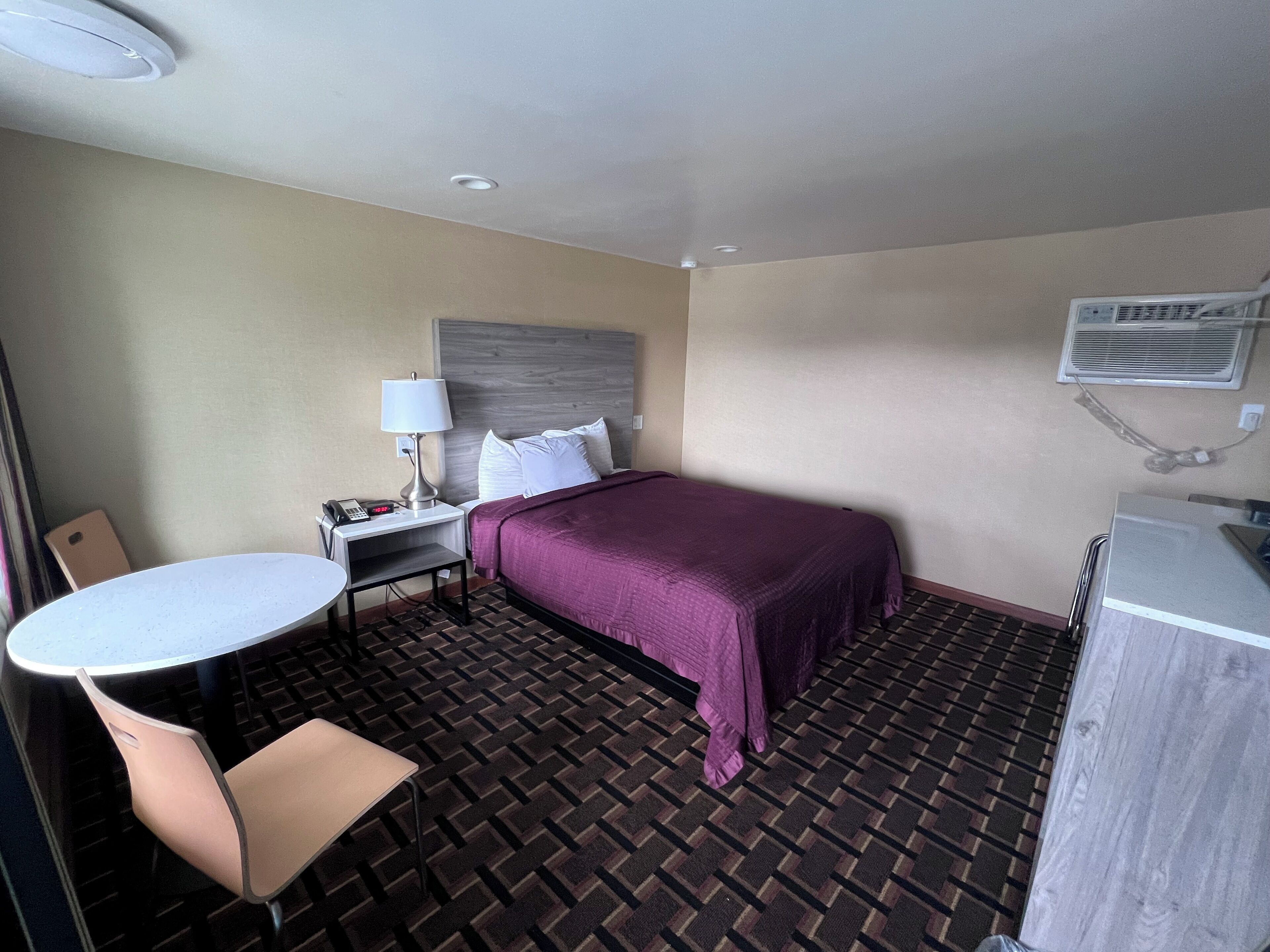 A hotel room with a bed, a desk with a lamp, a chair, and a small table.