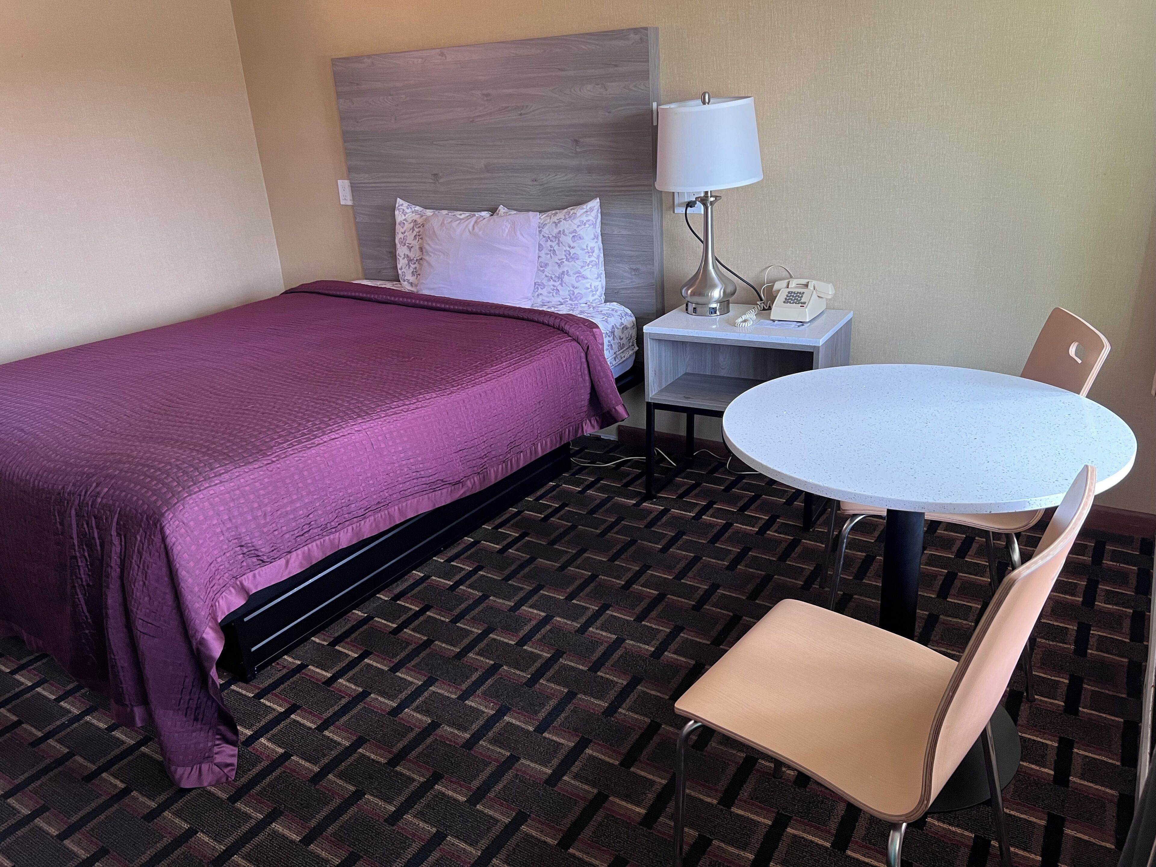 Una habitación de hotel con una cama, una mesita con una silla, una lámpara y un teléfono.