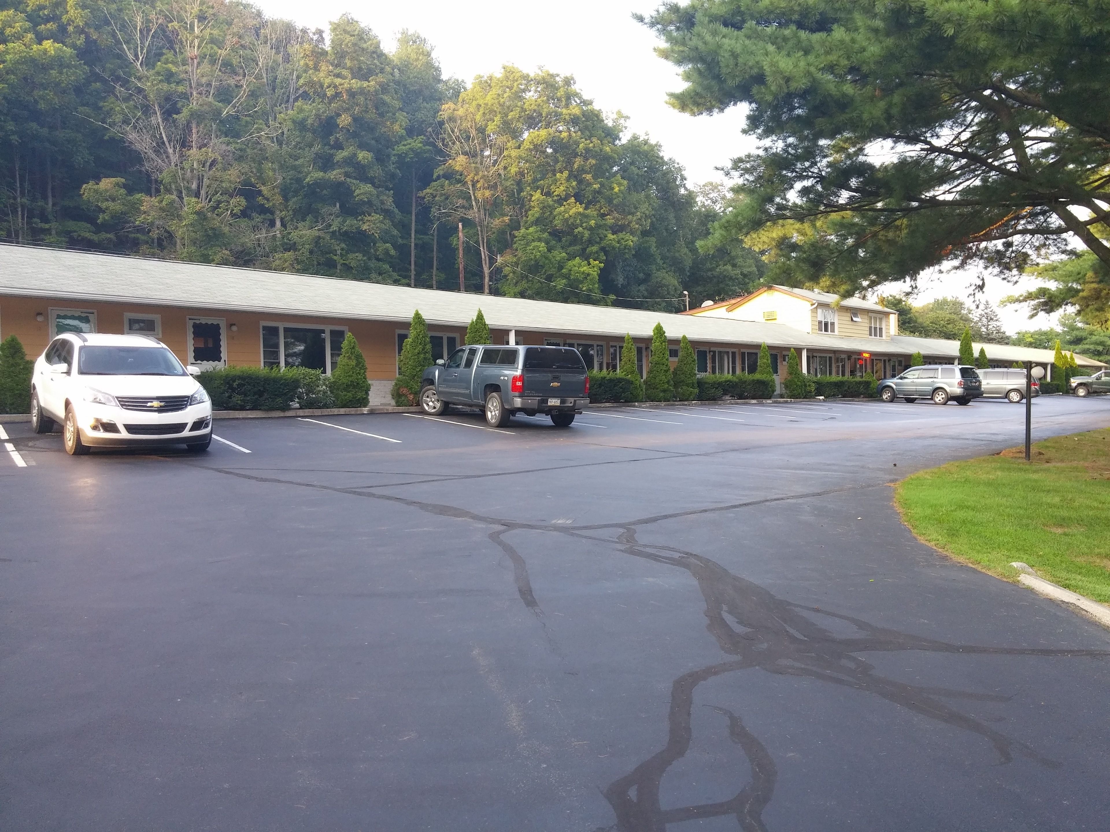 A parking lot with several vehicles, a building with a beige roof, and surrounding greenery.