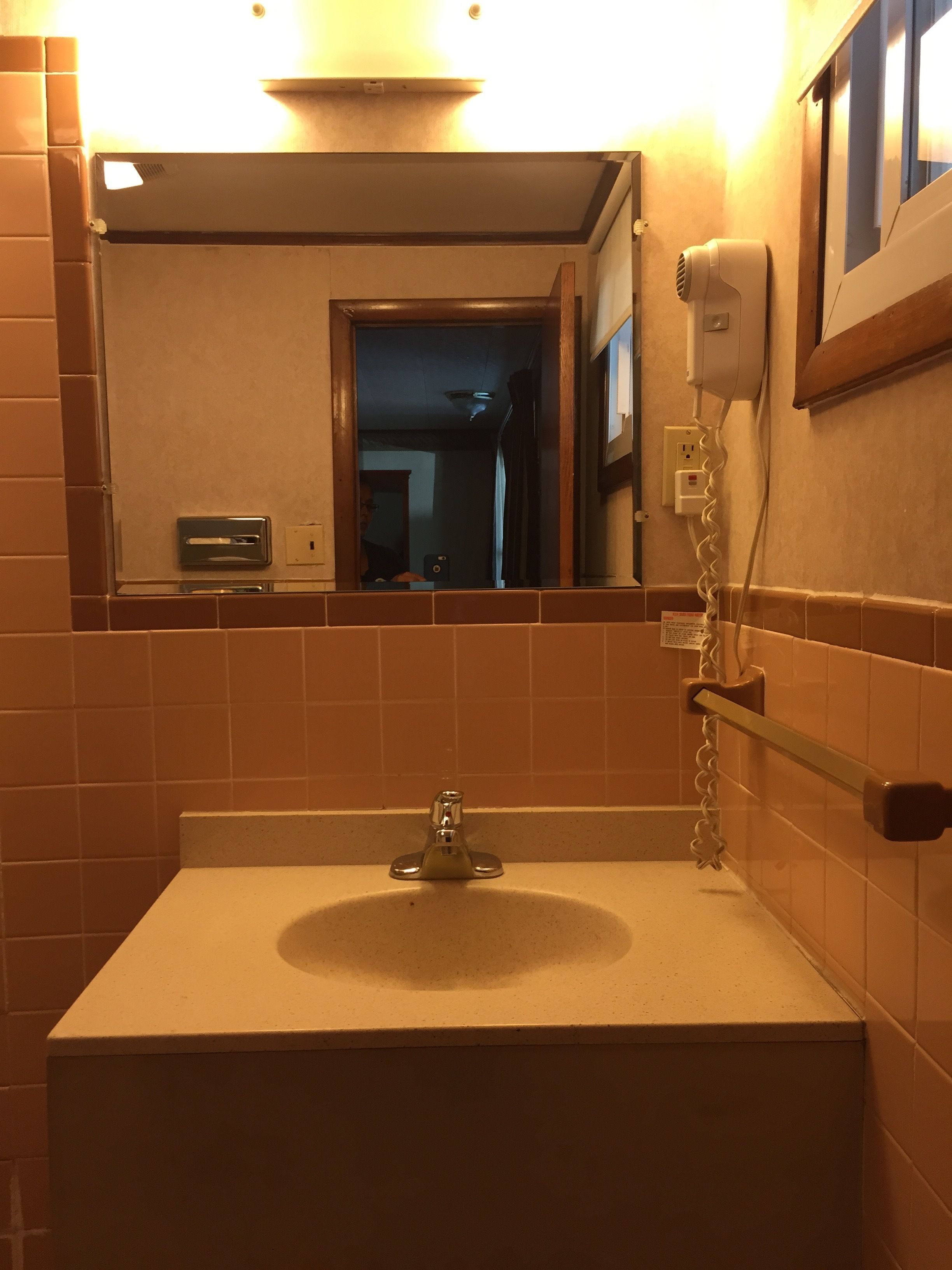 Un baño con lavamanos, espejo y secador de pelo en la pared.