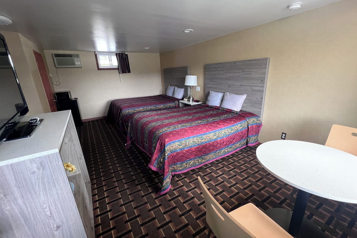 A hotel room with a bed, a desk, a chair, a small table, a lamp, and a window.
