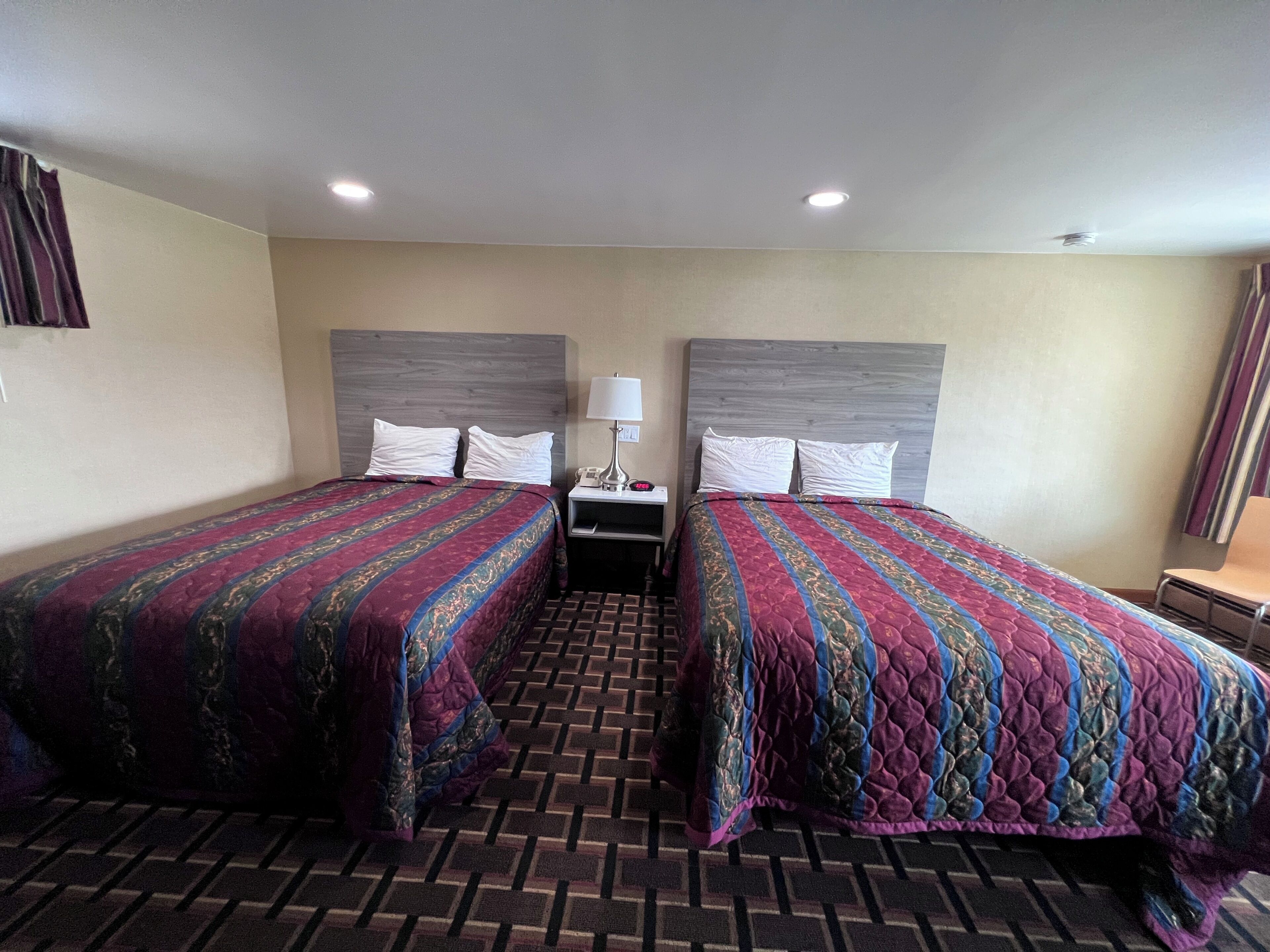 Een hotelkamer met twee bedden, een nachtkastje, een lamp en een kamerbreed tapijt met dessin.