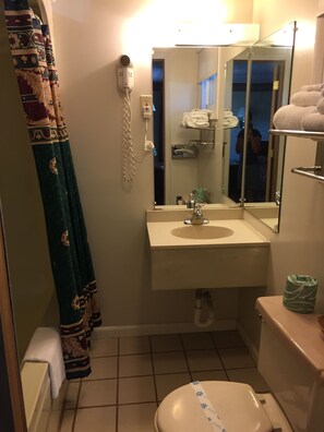 Casa de banho com lavatório, sanita e espelho. Tem um porta-toalhas com toalhas e um secador de cabelo na parede.