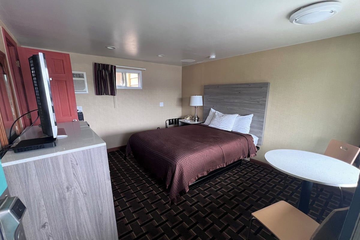 A hotel room with a bed, a desk with a computer, a chair, a table, and a window.