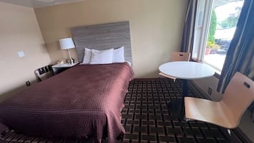 Une chambre d’hôtel avec un lit, un bureau doté d’une lampe, une table ronde et une chaise.