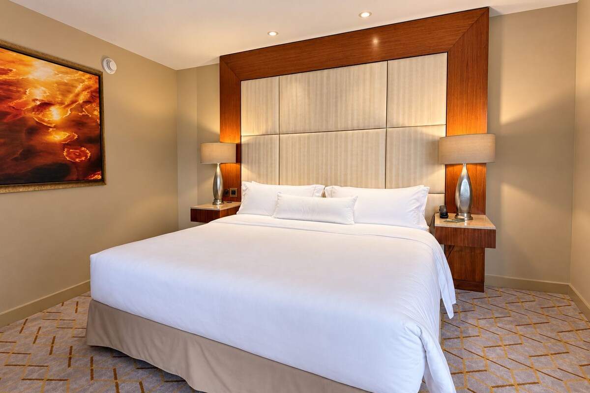 Een hotelkamer met een groot bed, twee nachtkastjes, een hoofdeinde en een schilderij aan de muur.