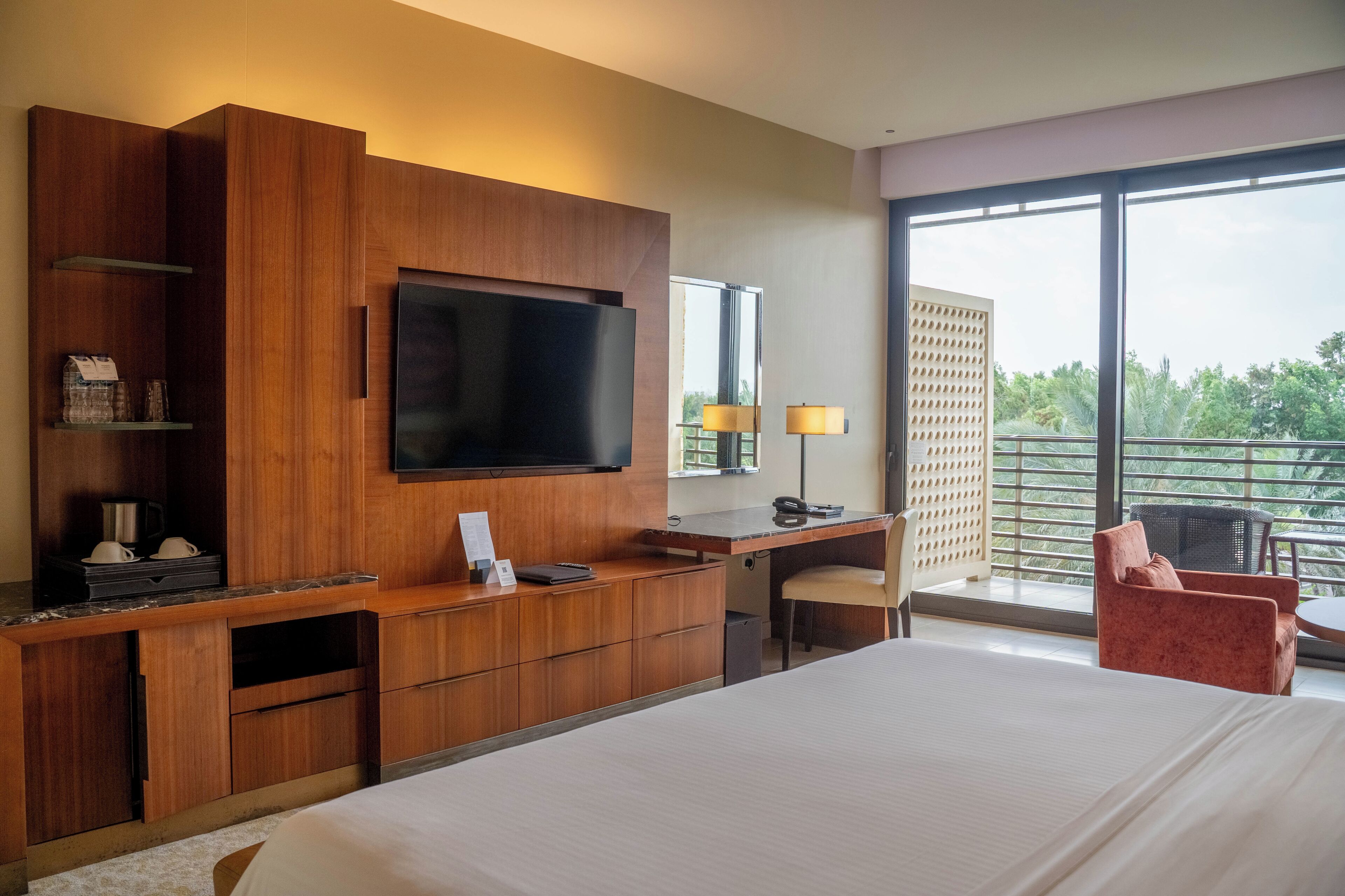 Een hotelkamer met een groot bed, een houten bureau, een flatscreen televisie en een balkon met uitzicht.