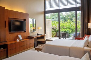 Habitación de hotel con dos camas, un escritorio, un televisor y vistas al jardín.