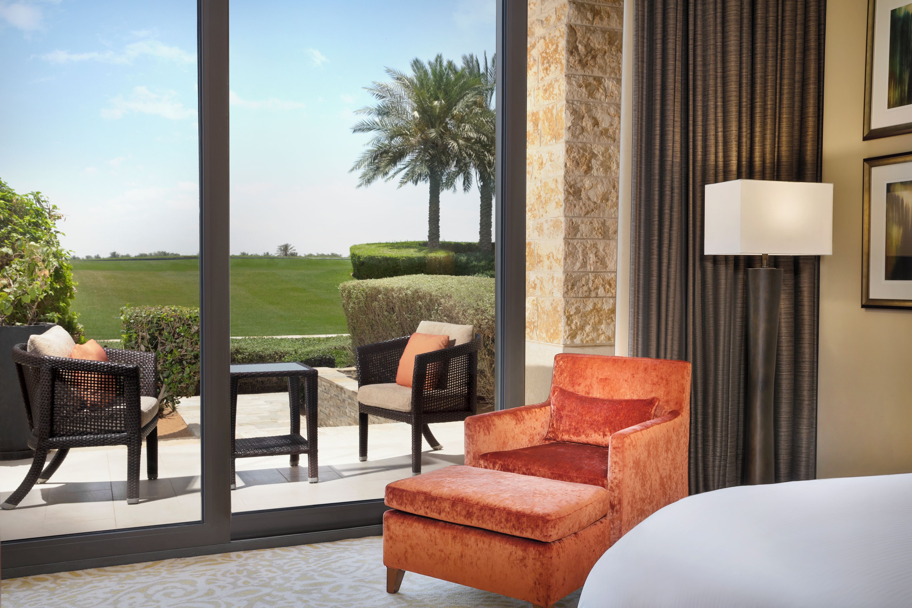 A hotel room with a large window, a bed, a chair, a table, and a lamp.