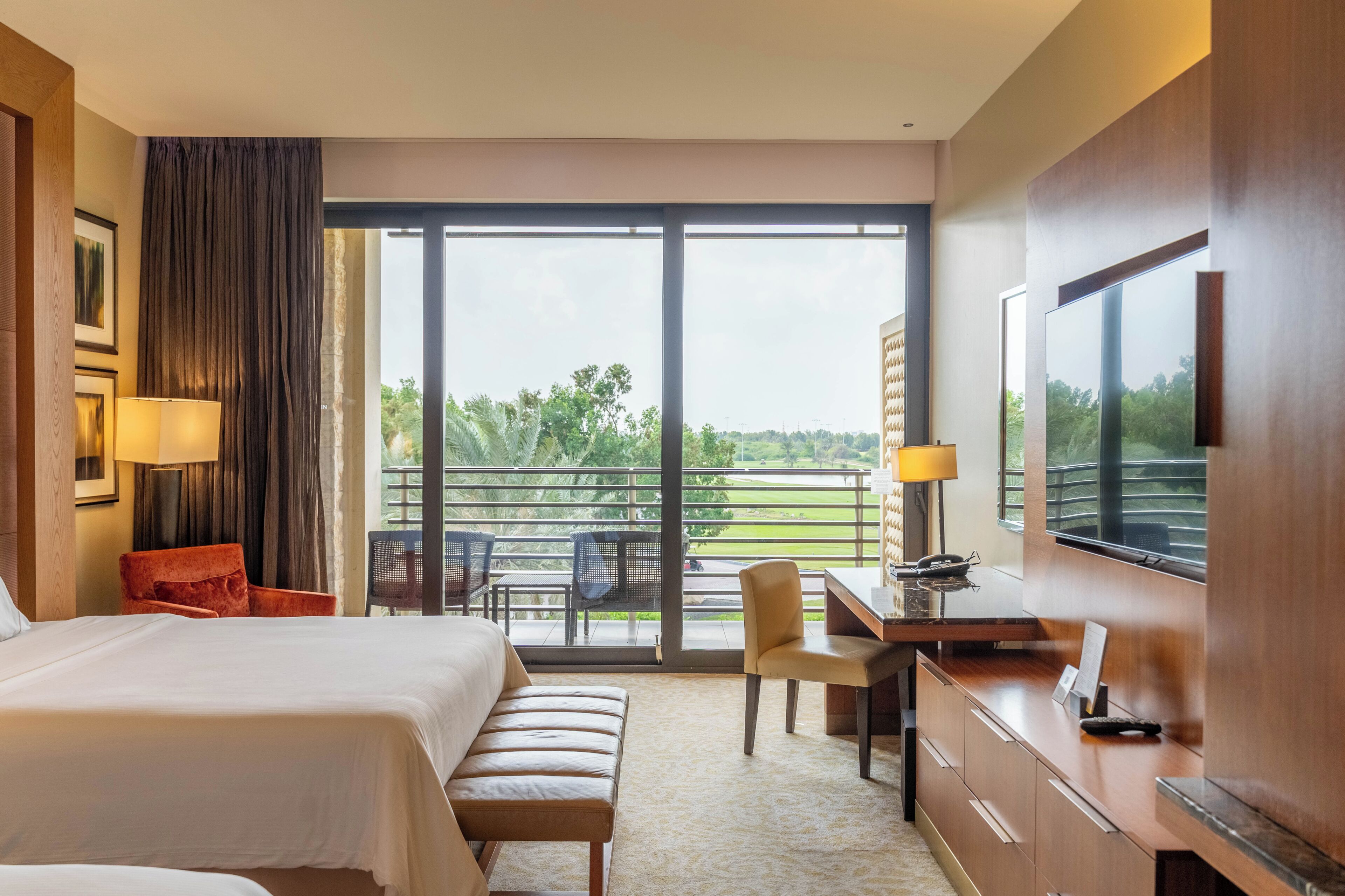 Habitación de hotel con cama, escritorio, sillas, televisor y balcón con vistas.