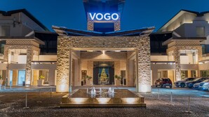 Ein Hotel Eingang mit einem auffälligen "VOGO" Schild, einer zentralen Fontäne und einem Parkplatz mit mehreren Autos.