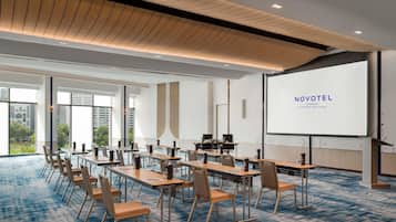 Ein moderner Hotelkonferenzraum mit einer großen Leinwand, auf der 'NOVOTEL Bangkok Platinum Pratunam' angezeigt wird.